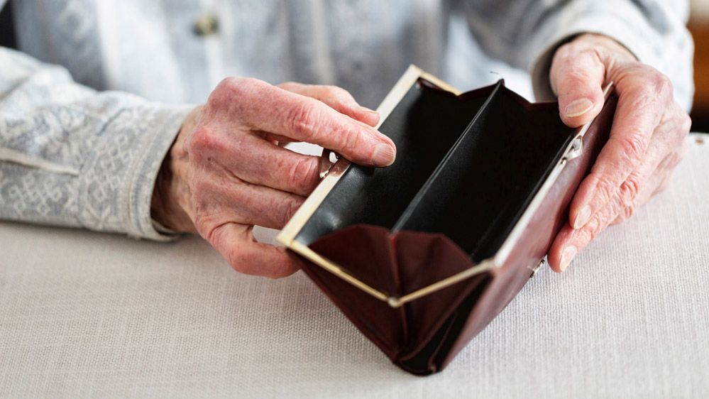Hände einer älteren Frau öffnen ein Portemonnaie.