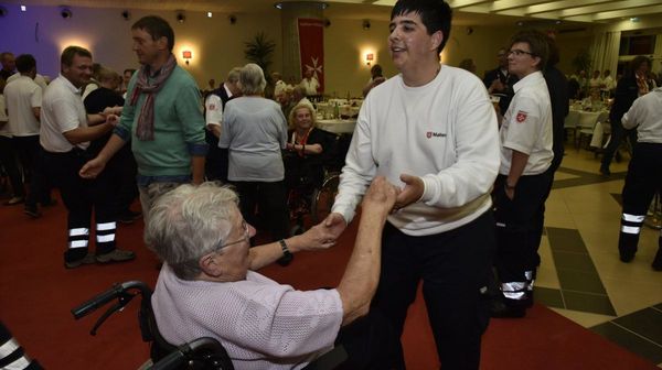 Eine Rollstuhlfahrerin tanzt mit einem Mann in einem Malteser-Pullover.
