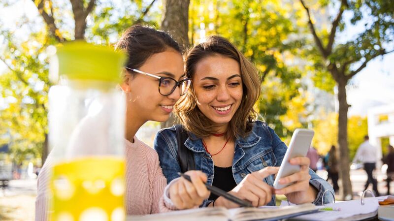 Zwei junge Frauen sitzen im Café und schauen auf ein Smartphone.