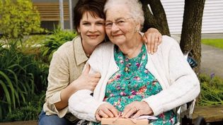 Eine jüngere Frau umarmt eine ältere Frau liebevoll. Beide lächeln in die Kamera.