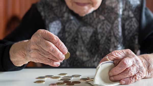 Ältere Frau sitzt am Tisch und zählt das Geld in ihrer Brieftasche.