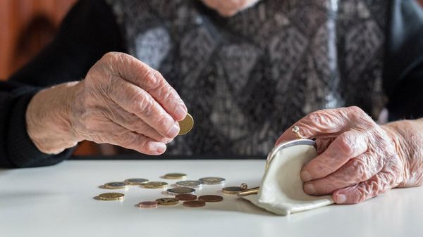 Ältere Frau sitzt am Tisch und zählt das Geld in ihrer Brieftasche.