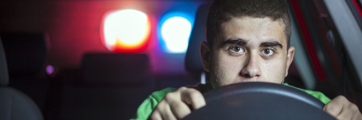Junger Mann am Steuer eines Autos mit Blaulicht im Hintergrund.