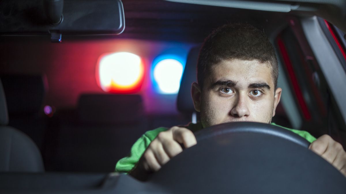 Junger Mann am Steuer eines Autos mit Blaulicht im Hintergrund.