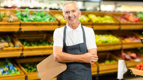 Ein Rentner, welcher im Supermarkt arbeitet lächelt.