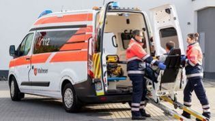 Zwei Mitarbeiter der Malteser tragen einen Patienten auf einer Trage in einen Krankentransportwagen (KTW).