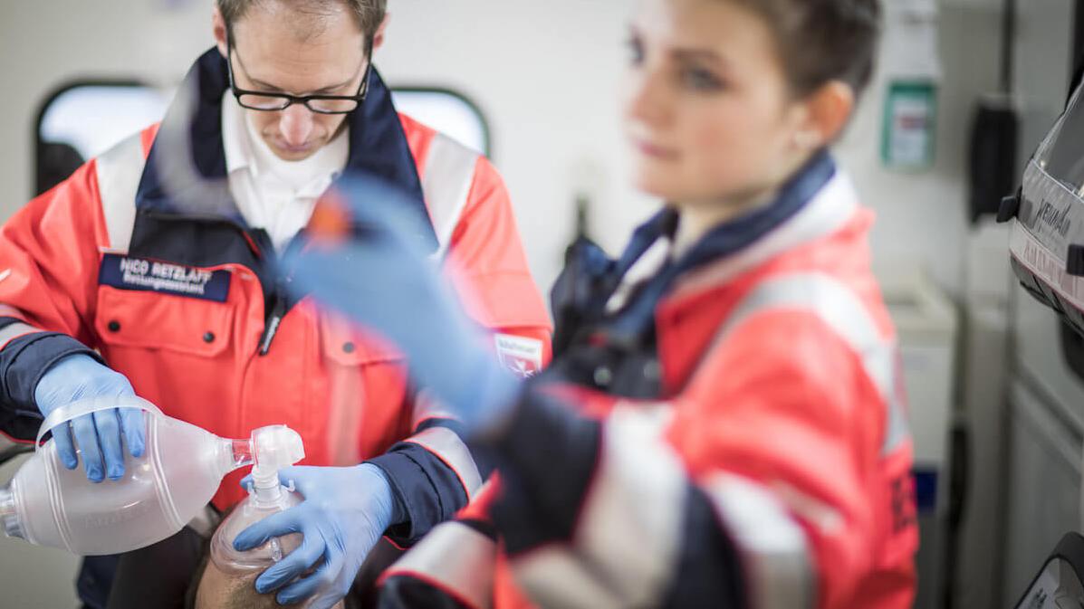 Zwei Notfallsanitäter legen einem Patienten im Krankenwagen eine Beatmungsmaske auf