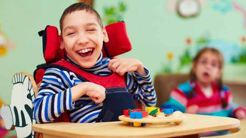 Ein lachender Junge in einem Rollstuhl mit Sicherheitsgurt