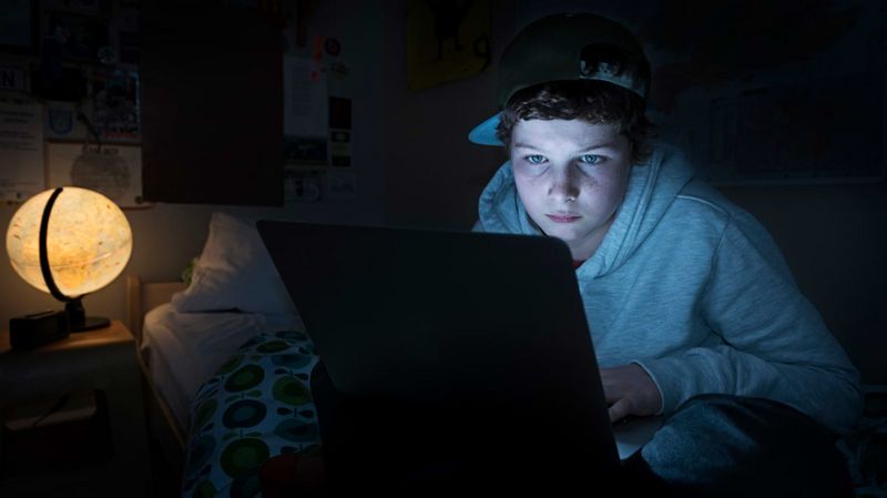Ein Junge in einem dunklen Raum vor einem Laptop