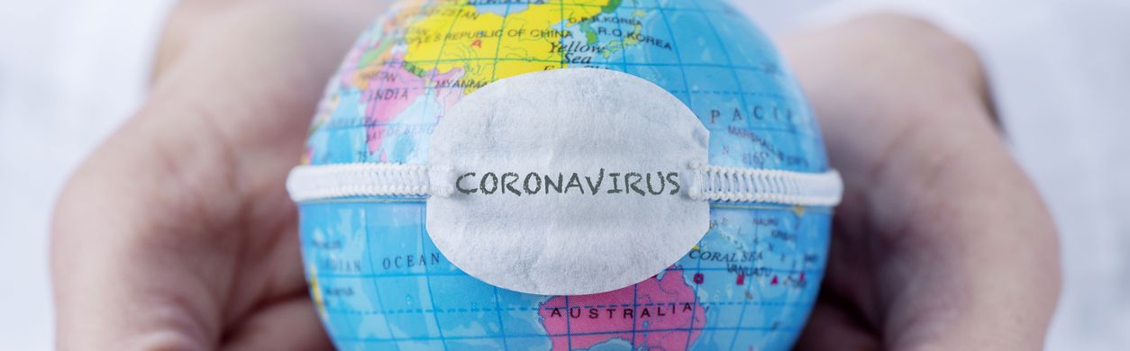 Hände halten eine Weltkugel, um die ein Mund-Nasen-Schutz mit der Aufschrift „Coronavirus“ gespannt ist.